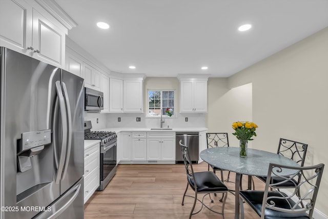 kitchen with a sink, stainless steel appliances, light countertops, light wood-style floors, and white cabinetry