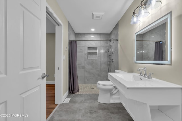 bathroom with baseboards, visible vents, tiled shower, a sink, and toilet