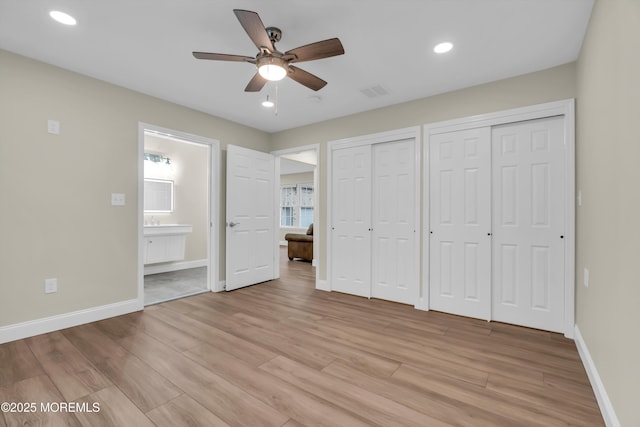 unfurnished bedroom featuring light wood-style flooring, baseboards, visible vents, and two closets