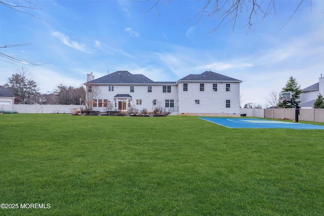 rear view of house featuring a yard, basketball court, and fence