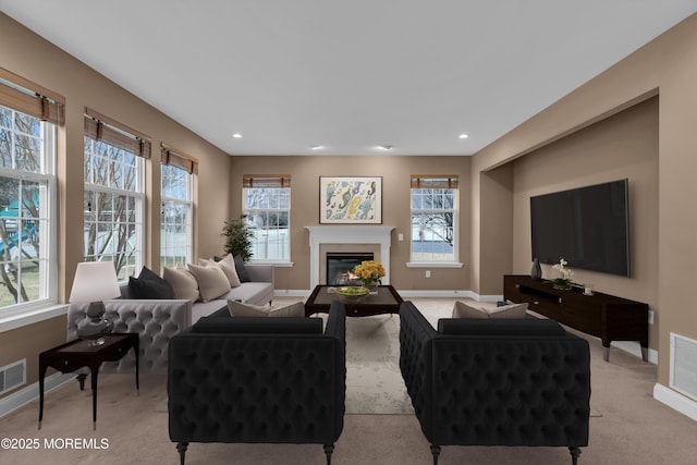 living area featuring a glass covered fireplace, recessed lighting, light colored carpet, and baseboards