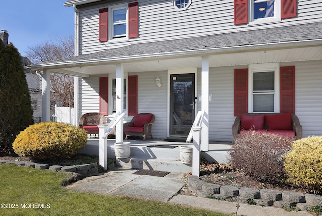 view of exterior entry with roof with shingles and covered porch