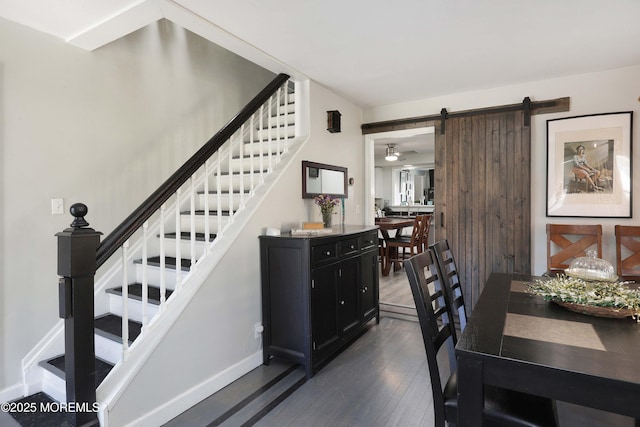 dining space featuring a barn door, baseboards, dark wood finished floors, and stairs