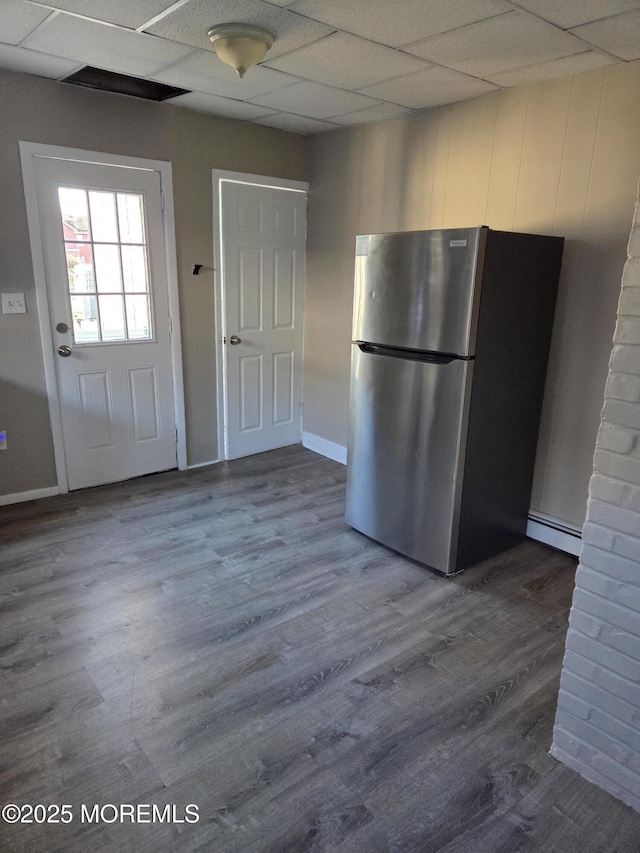 kitchen with a drop ceiling, a baseboard heating unit, dark wood finished floors, freestanding refrigerator, and baseboards