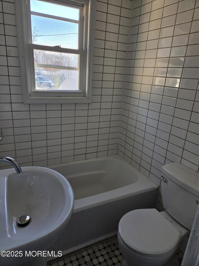 bathroom with a washtub, toilet, tile walls, and a sink