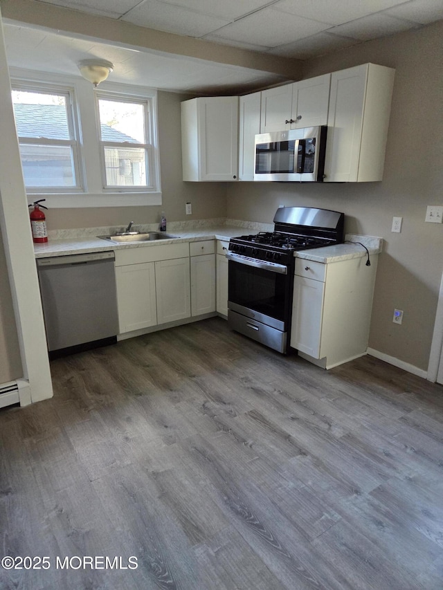 kitchen with a sink, stainless steel appliances, wood finished floors, and white cabinets