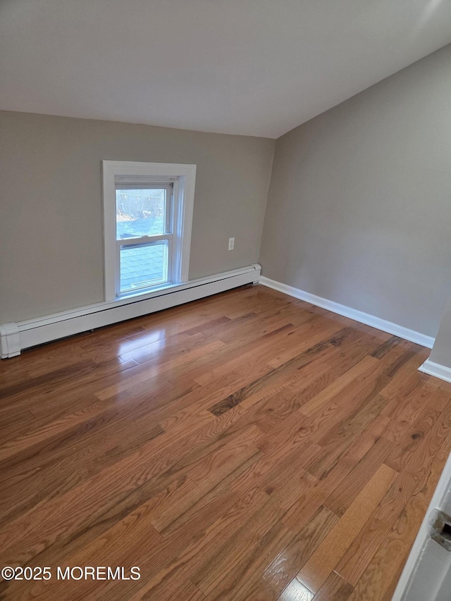 empty room featuring a baseboard heating unit, baseboards, and wood finished floors