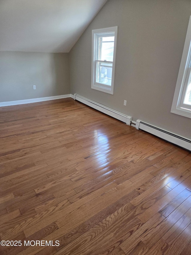 additional living space with a baseboard heating unit, lofted ceiling, wood finished floors, and a wealth of natural light