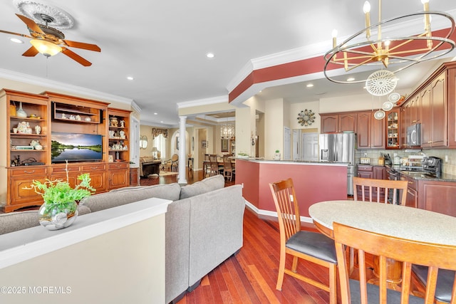 living area with ornamental molding, recessed lighting, ceiling fan with notable chandelier, wood finished floors, and ornate columns