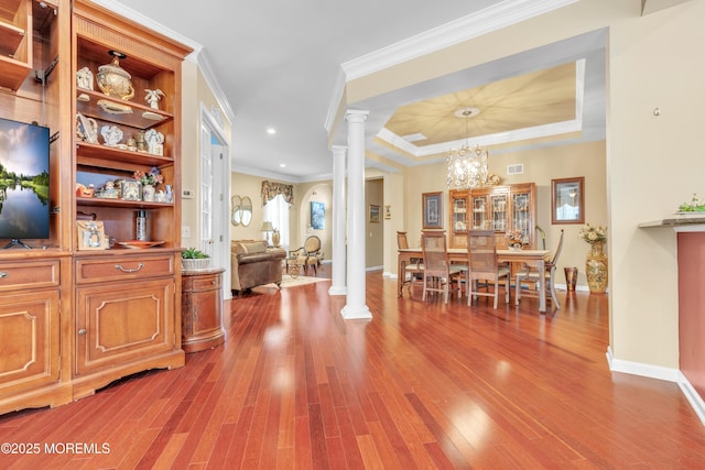 dining room featuring visible vents, wood finished floors, crown molding, a raised ceiling, and ornate columns