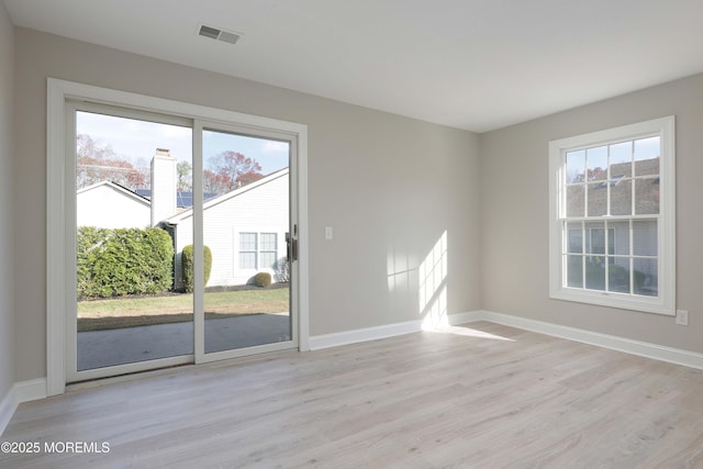 spare room featuring baseboards, a healthy amount of sunlight, visible vents, and light wood-type flooring