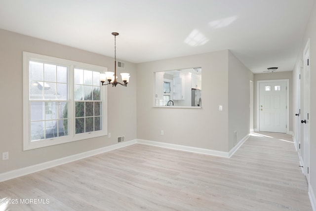 unfurnished dining area featuring an inviting chandelier, light wood-style floors, visible vents, and baseboards