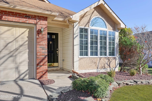 view of exterior entry featuring brick siding, roof with shingles, and an attached garage