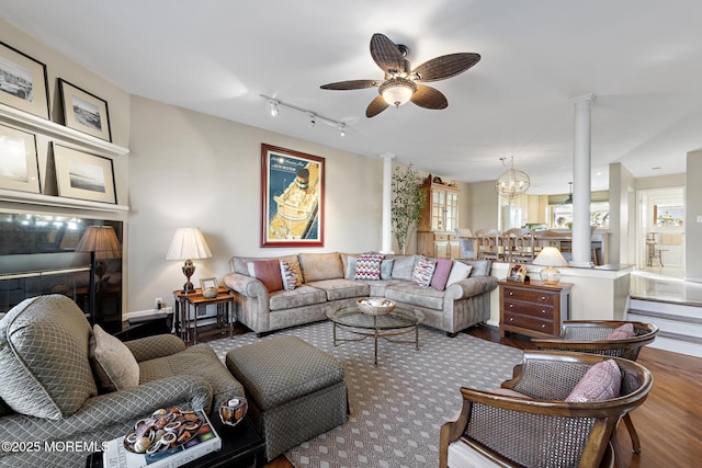 living room with ceiling fan with notable chandelier, wood finished floors, and ornate columns