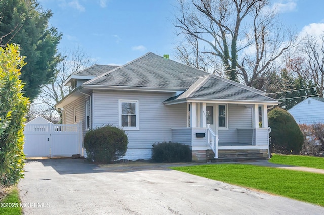 bungalow-style home with a porch, a shingled roof, a front yard, and a gate