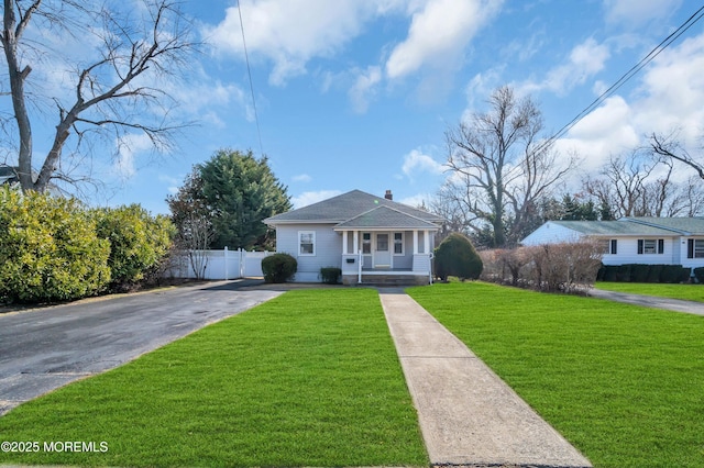 bungalow-style home featuring a porch, driveway, a front lawn, and fence