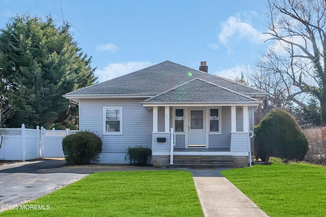 bungalow-style home featuring a porch, fence, a front yard, a shingled roof, and a chimney