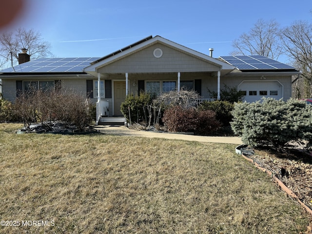 ranch-style house featuring a front lawn, a porch, roof mounted solar panels, a chimney, and a garage