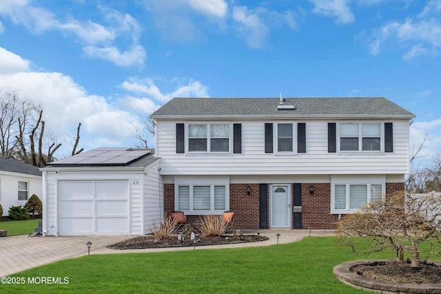 colonial-style house with brick siding, a front yard, roof mounted solar panels, decorative driveway, and a garage