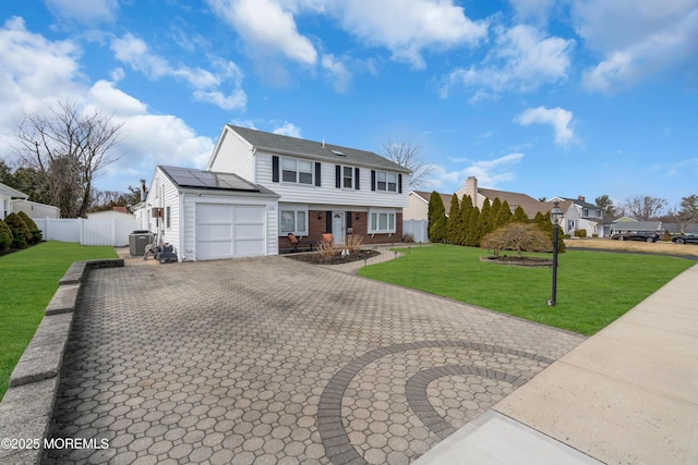 colonial house with decorative driveway, roof mounted solar panels, a front yard, a garage, and brick siding