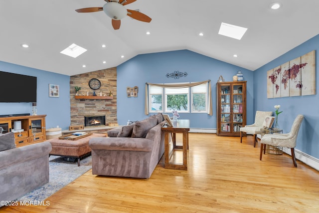 living room featuring light wood-type flooring, a baseboard heating unit, lofted ceiling with skylight, and a stone fireplace