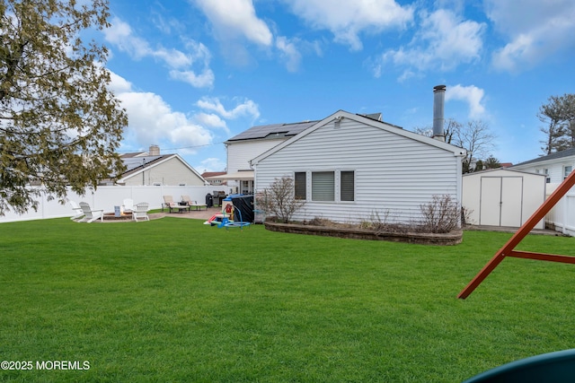 rear view of property with a fire pit, a shed, a fenced backyard, a patio area, and an outbuilding