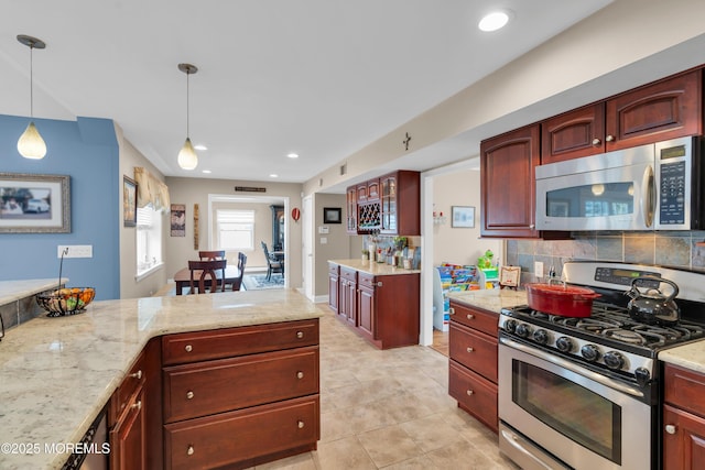 kitchen featuring tasteful backsplash, pendant lighting, light stone counters, appliances with stainless steel finishes, and reddish brown cabinets