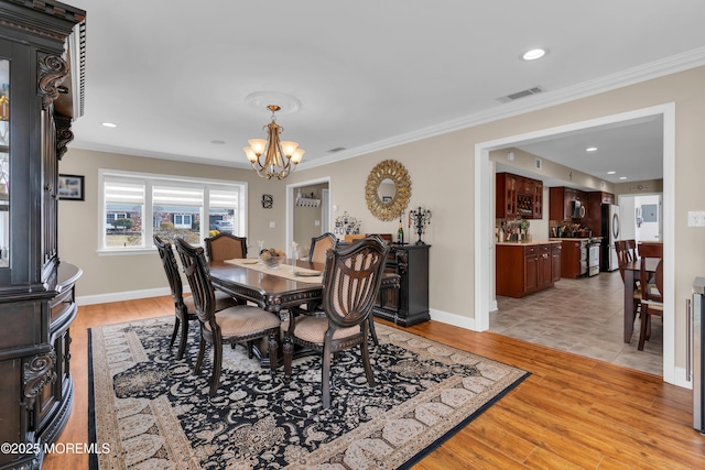 dining room featuring an inviting chandelier, crown molding, visible vents, and light wood-type flooring