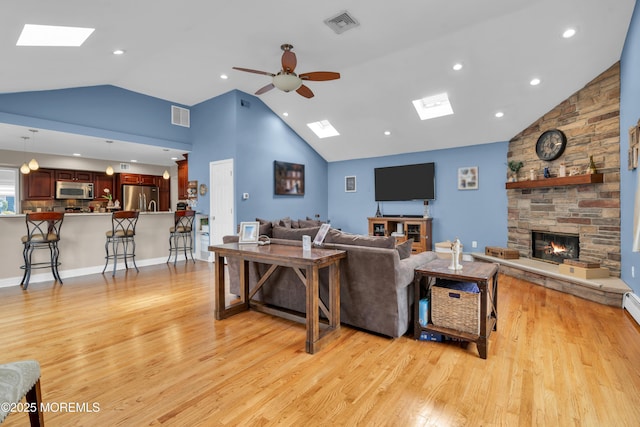 living room with light wood-type flooring, visible vents, a skylight, and a fireplace