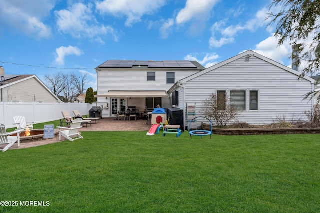 back of house with a fenced backyard, a yard, a fire pit, solar panels, and a patio area