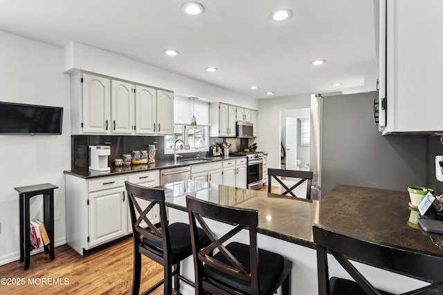 kitchen featuring a sink, dark countertops, recessed lighting, light wood-style floors, and appliances with stainless steel finishes