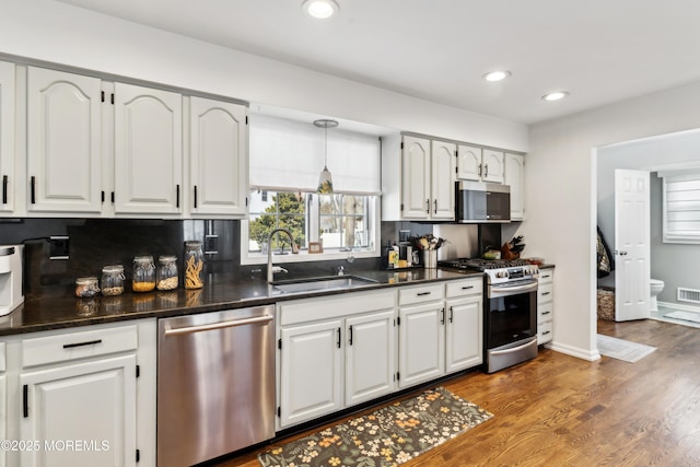 kitchen with a sink, dark countertops, wood finished floors, recessed lighting, and appliances with stainless steel finishes