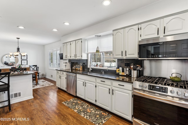 kitchen featuring dark countertops, visible vents, appliances with stainless steel finishes, hanging light fixtures, and a sink