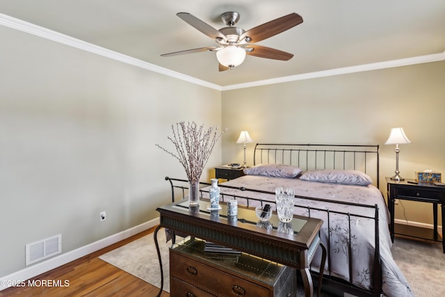 bedroom featuring wood finished floors, baseboards, visible vents, ceiling fan, and crown molding