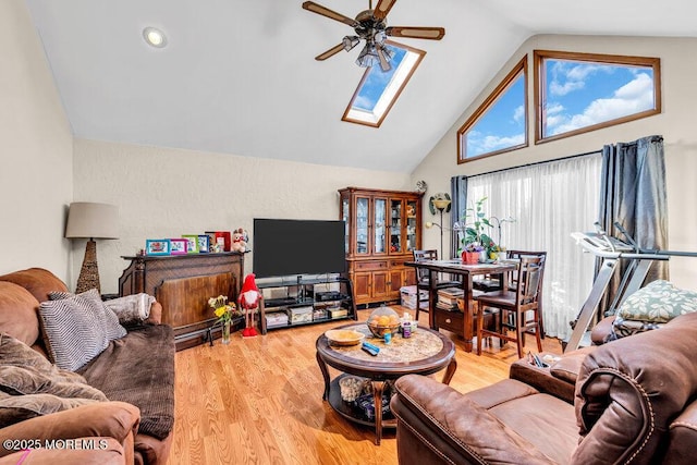 living room featuring light wood finished floors, high vaulted ceiling, a skylight, and a ceiling fan