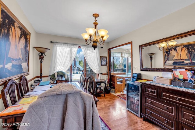 dining space with an inviting chandelier, wine cooler, light wood-type flooring, and a dry bar