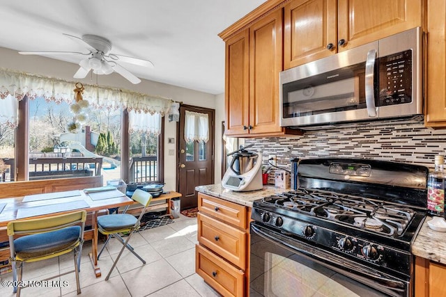 kitchen with stainless steel microwave, light stone counters, black gas range oven, and tasteful backsplash