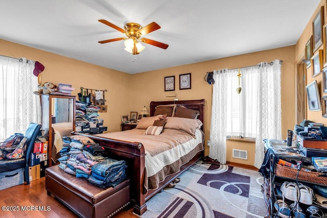 bedroom with visible vents, multiple windows, wood finished floors, and a ceiling fan