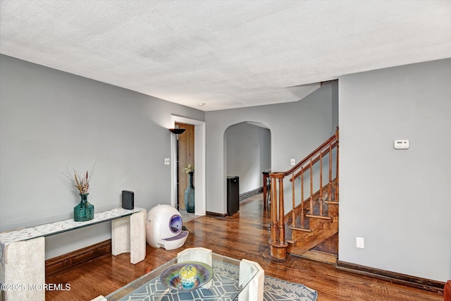 interior space with a textured ceiling, wood finished floors, stairway, arched walkways, and baseboards