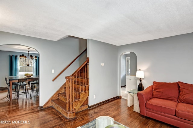 living area with a notable chandelier, a textured ceiling, wood finished floors, stairway, and arched walkways