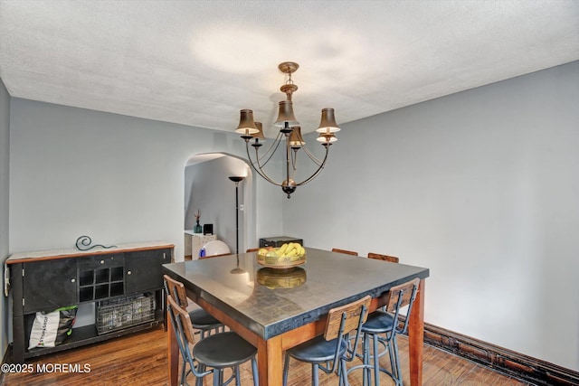 dining area featuring arched walkways, dark wood-type flooring, an inviting chandelier, and a textured ceiling