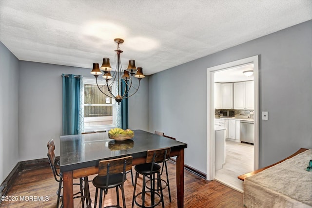 dining room featuring a notable chandelier, a textured ceiling, baseboards, and wood finished floors