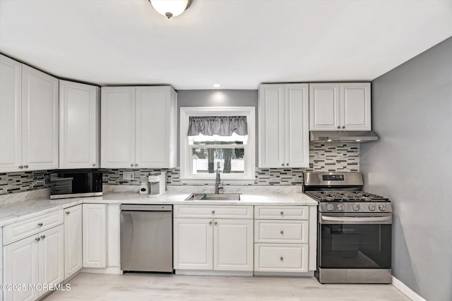 kitchen with tasteful backsplash, baseboards, under cabinet range hood, stainless steel appliances, and a sink