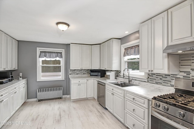 kitchen with under cabinet range hood, radiator heating unit, appliances with stainless steel finishes, white cabinets, and a sink