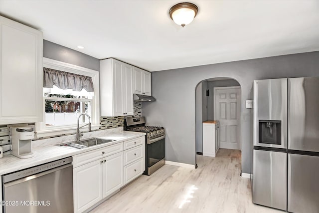 kitchen featuring arched walkways, a sink, stainless steel appliances, under cabinet range hood, and backsplash