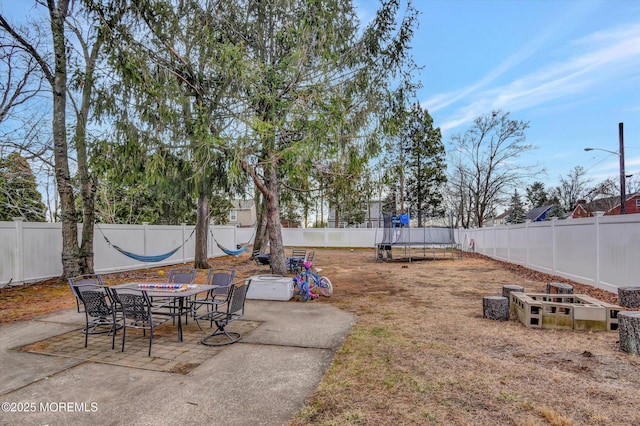 view of yard with a fenced backyard, a trampoline, outdoor dining space, and a patio area