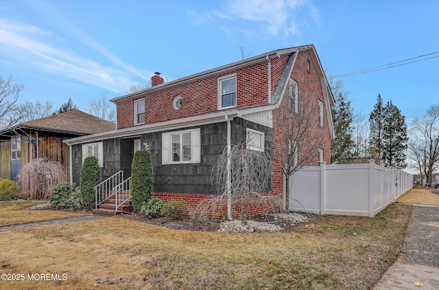 view of front facade with a front yard, fence, brick siding, and a chimney