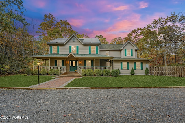 view of front of home featuring a yard, a porch, solar panels, and fence