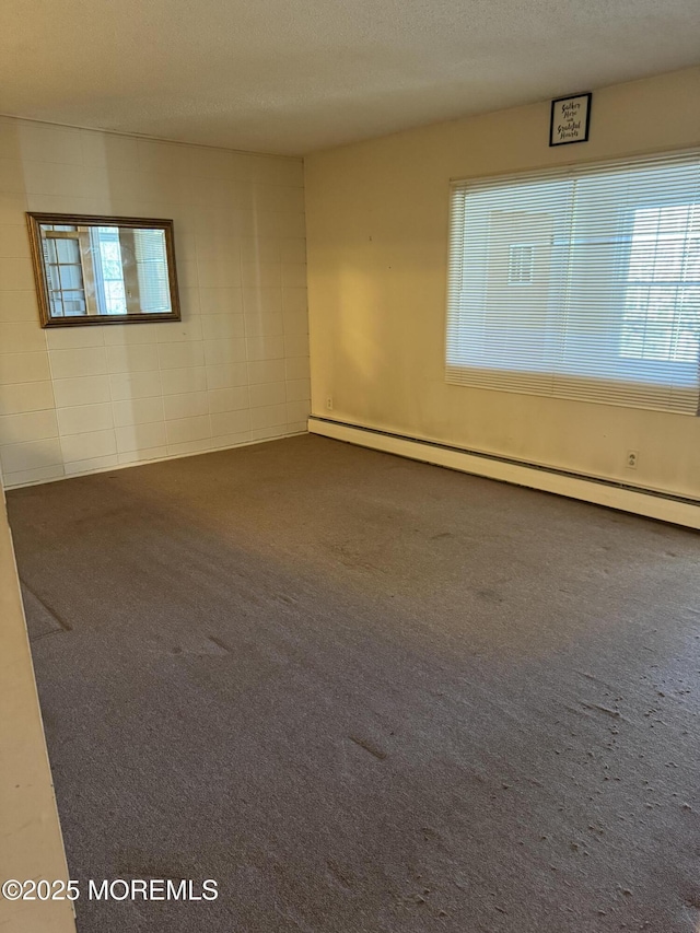 spare room featuring a baseboard heating unit, dark carpet, and a textured ceiling