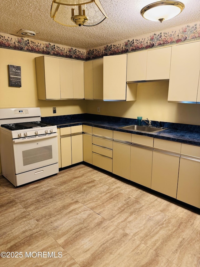 kitchen with a textured ceiling, dark countertops, white range with gas stovetop, and a sink